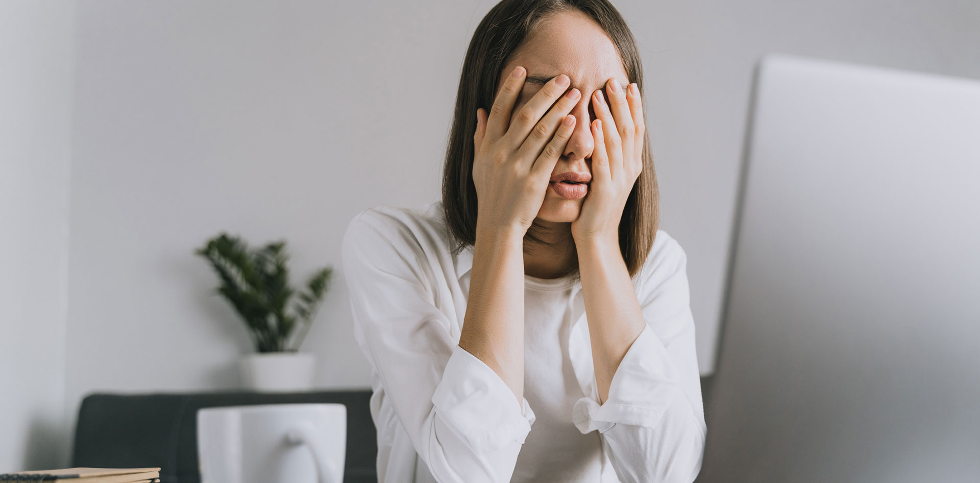 疲惫的女人用手捂着脸站在桌面显示器前