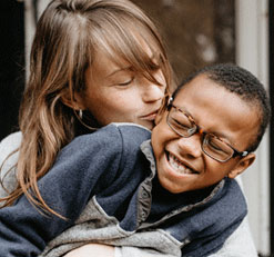 A photo of a woman kissing her son on his cheek.